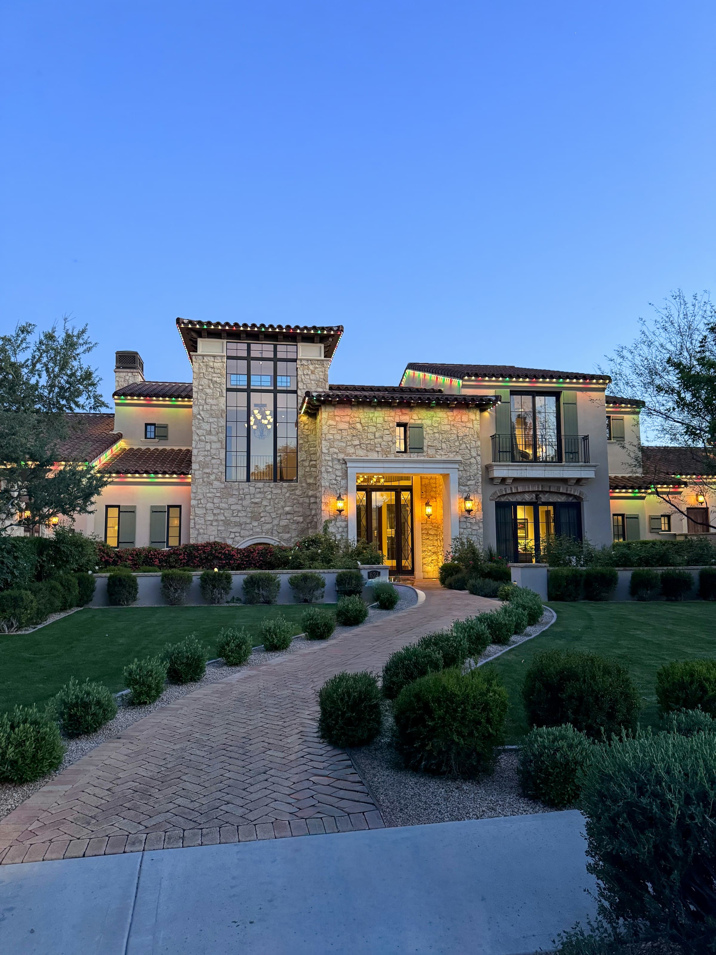 A home at dusk at the end of a long drive lined with low planting.