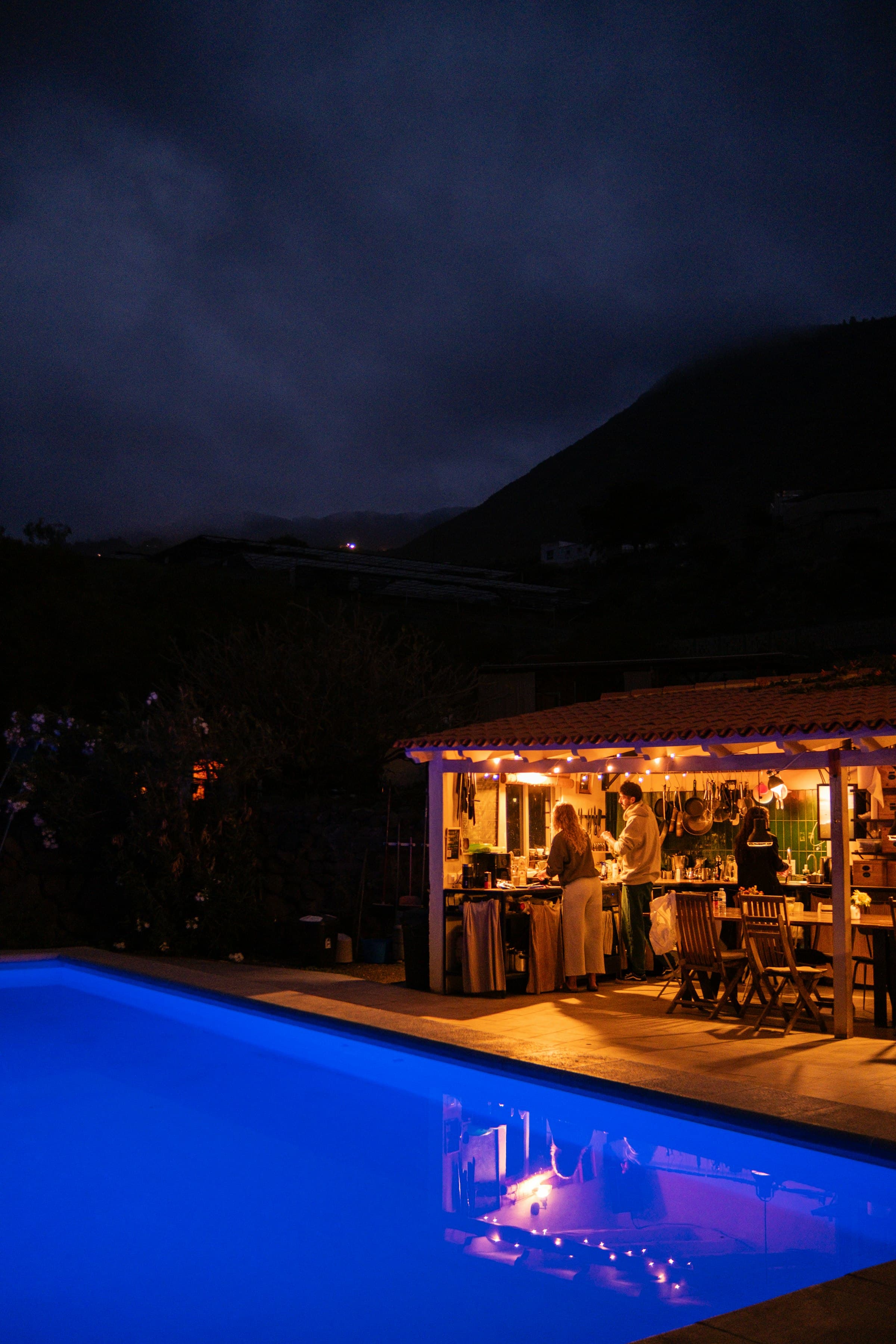 A bright blue pool at night in front of a lit covered patio.
