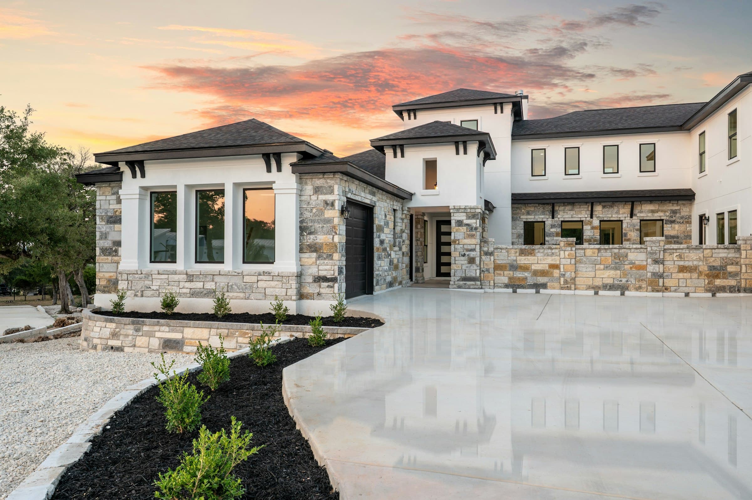 A new stone and stucco home at sunset with fresh landscaping along a curved drive.